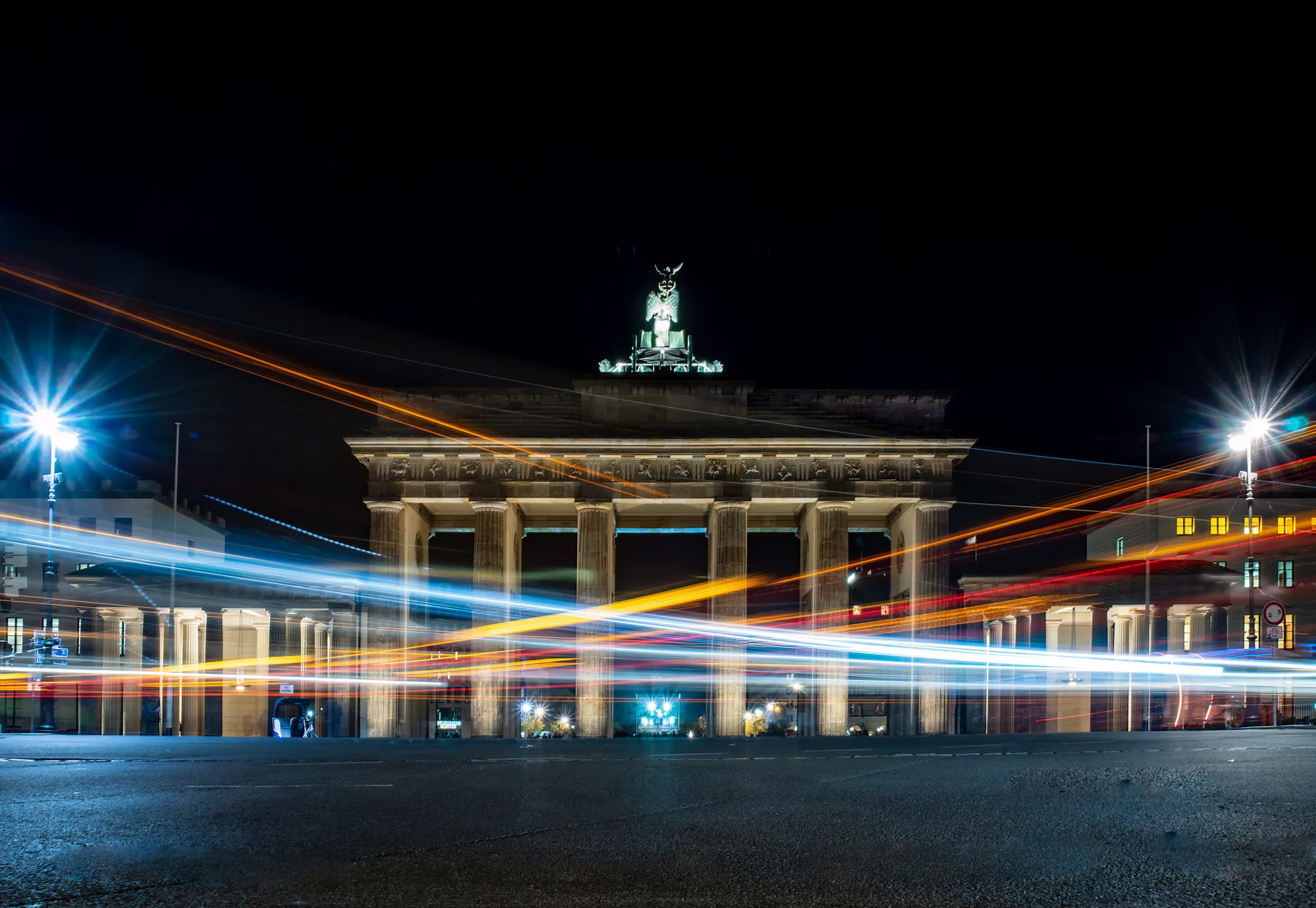 Brandenburger Tor bei Nacht, davor die Lichtspuren vorbeifahrender Fahrzeuge.