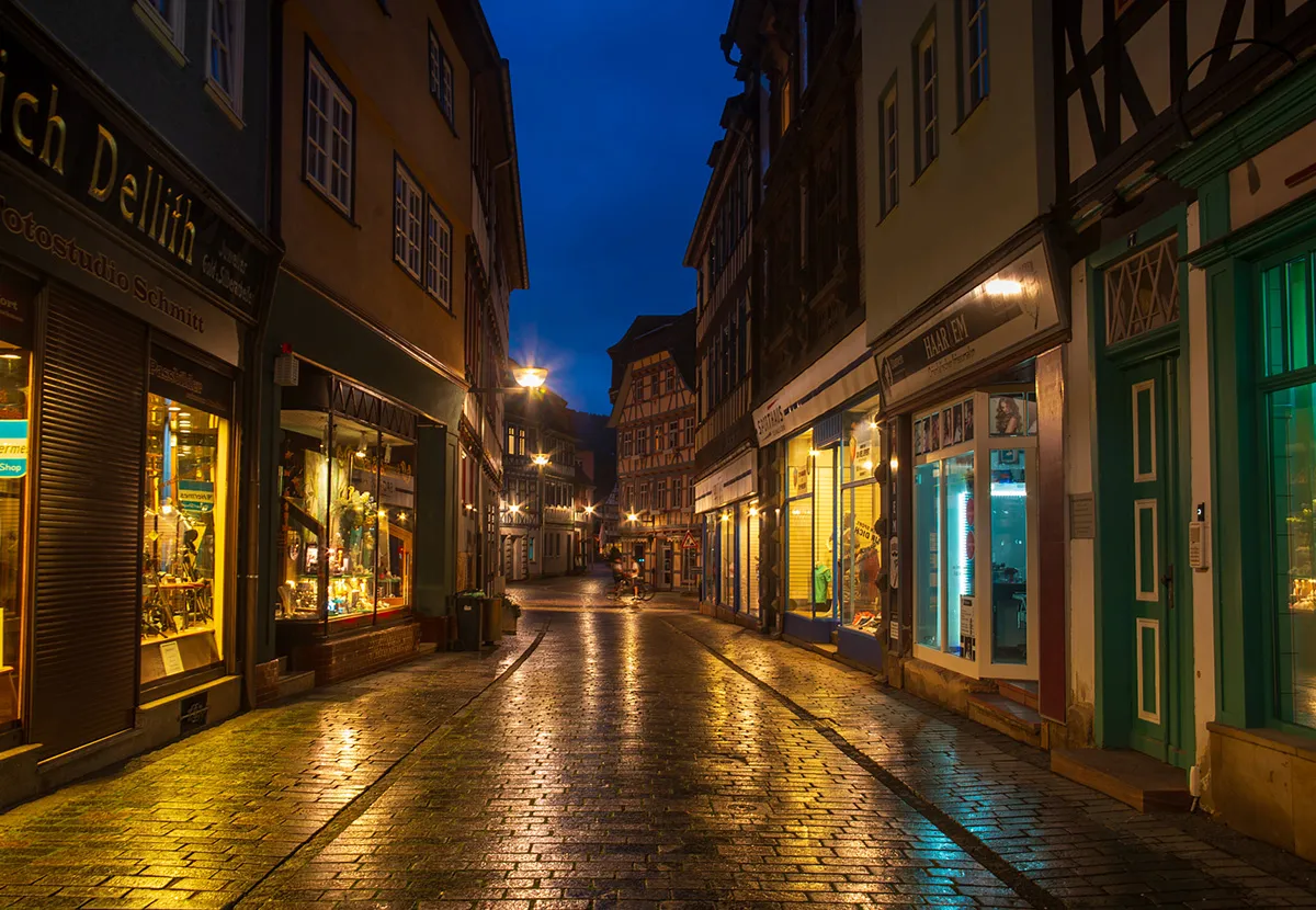 Fachwerkgasse in der blauen Stunde, nasses Kopfsteinpflaster spiegelt die Schaufensterlichter.