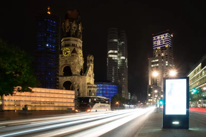Gedächtniskirche und Hochhäuser bei Nacht, davor die Lichtspuren des Verkehrs.