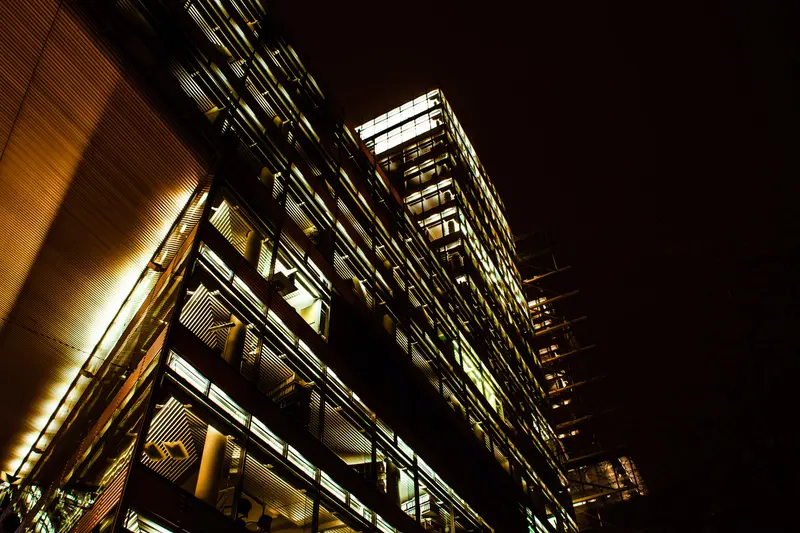 Untersicht auf eine beleuchtete Bürohausfassade bei Nacht.