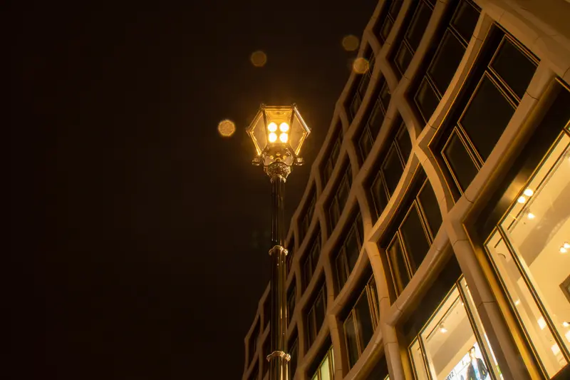 Straßenlaterne vor einer geschwungenen Glasfassade bei Nacht.
