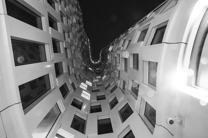 Schwarzweiß: Untersicht in einen Innenhof mit gewölbter Fensterfassade.