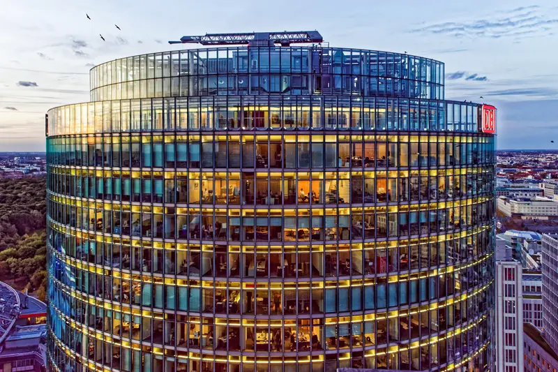 Rundes Bürogebäude mit farbig beleuchteter Glasfassade in der Dämmerung.