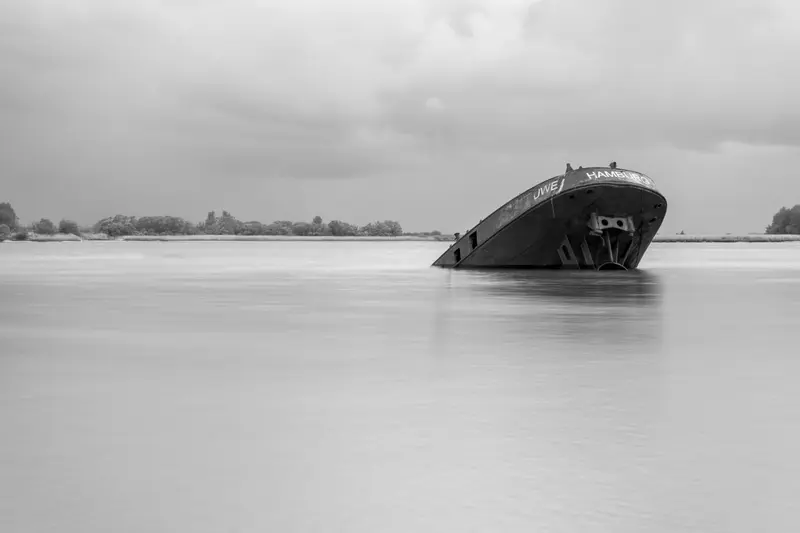 Schwarzweiß: gestrandetes Schiffswrack im flachen Wasser, in Langzeitbelichtung.