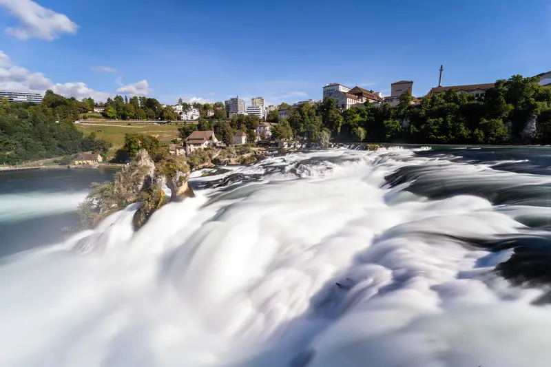 Langzeitbelichtung des Rheinfalls: Die Gischt verschwimmt zu weißen Schlieren, über dem Ufer stehen Schloss und Häuser.