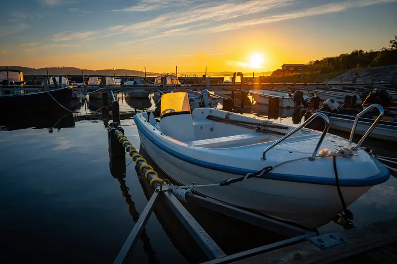 Boote am Steg im ersten Morgenlicht, die Sonne steht knapp über der Uferlinie.