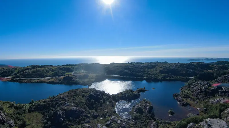 Luftbild einer felsigen Küstenlandschaft mit See, das Gegenlicht spiegelt sich im Wasser.