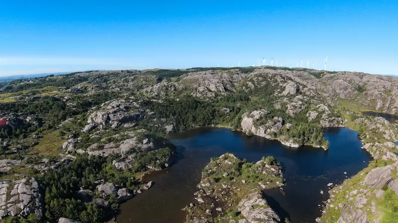 Luftbild: bewaldete Felskuppen rund um einen dunklen See.