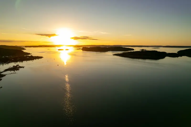 Luftbild über dem Wasser bei Sonnenuntergang, die Sonne zieht eine helle Bahn.