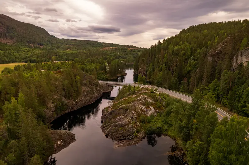 Luftbild eines Flusstals mit Brücke und Straße unter tiefhängenden Wolken.