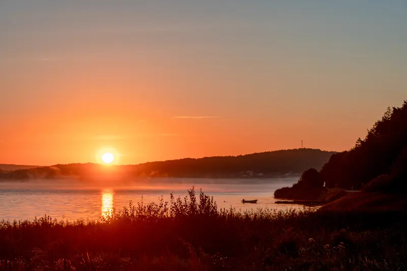 Kräftiger Sonnenuntergang über dem Fjord, rot verfärbte Vegetation im Vordergrund.