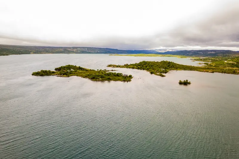Luftbild einer flachen Insel in einem See, ringsum helle Untiefen.