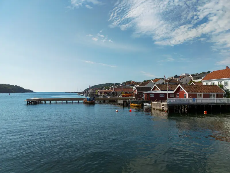 Steg und rote Häuser am Wasser unter blauem Himmel.