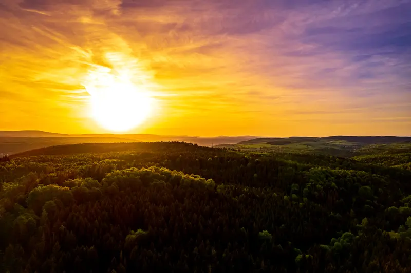 Sonnenuntergang über bewaldeten Hügeln, von oben gesehen.