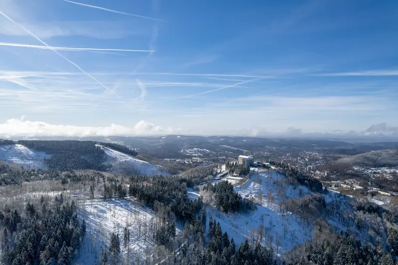 Verschneite Bergrücken von oben, am Horizont eine Ortschaft.