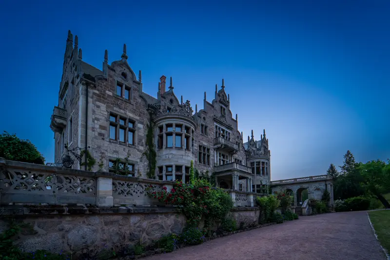 Schloss im neugotischen Stil in der blauen Stunde, davor die Terrasse.