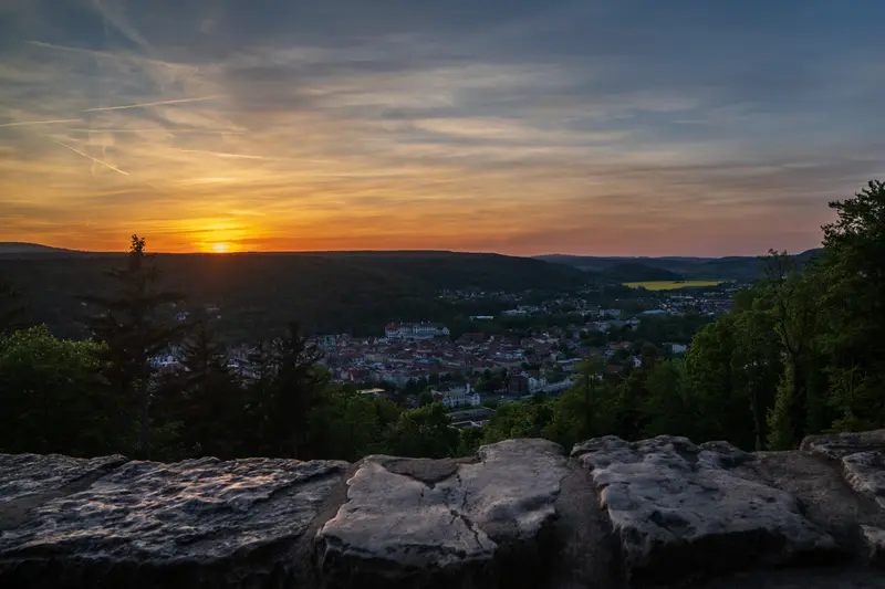 Sonnenuntergang über bewaldeten Höhen, im Vordergrund eine Felskante.