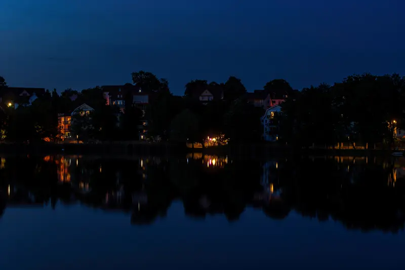 Stiller See in der Dämmerung, die Uferbebauung spiegelt sich im Wasser.
