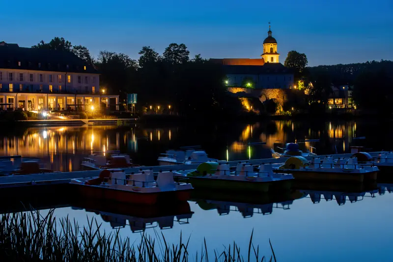 Kurhaus und Kirche am Seeufer bei Nacht, im Vordergrund Tretboote.