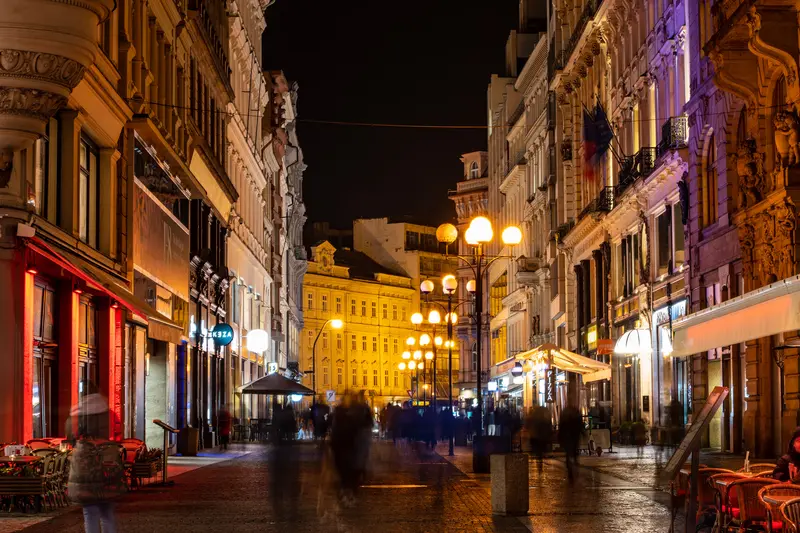 Enge Gasse mit beleuchteten Geschäften und Straßenlaternen bei Nacht.