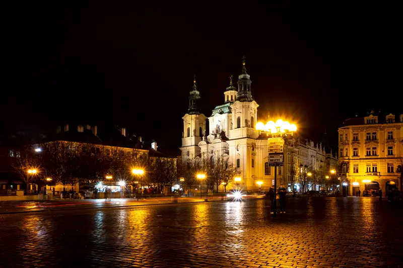 Die Nikolauskirche bei Nacht, davor nasses Kopfsteinpflaster mit Spiegelungen.